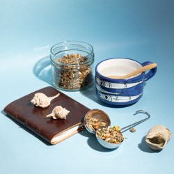 Fleurs de CBD dans boule à infusion à côté d'une tasse sur fond bleu ciel