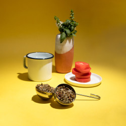 Fleurs de CBD dans boule à infusion à côté d'une tasse sur fond jaune